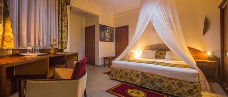 A hotel room with a bed, a desk, a chair, a nightstand, and a bedside table.