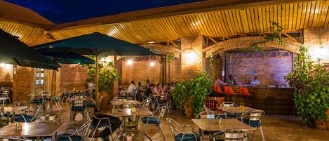 An outdoor dining area with brick walls, wooden ceiling, and metal chairs.