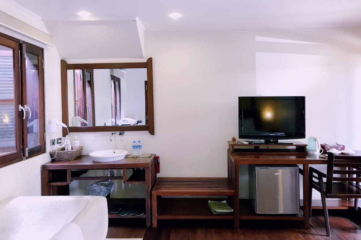A hotel room with a wooden vanity, a sink, a mirror, a television, a small refrigerator, and a chair.