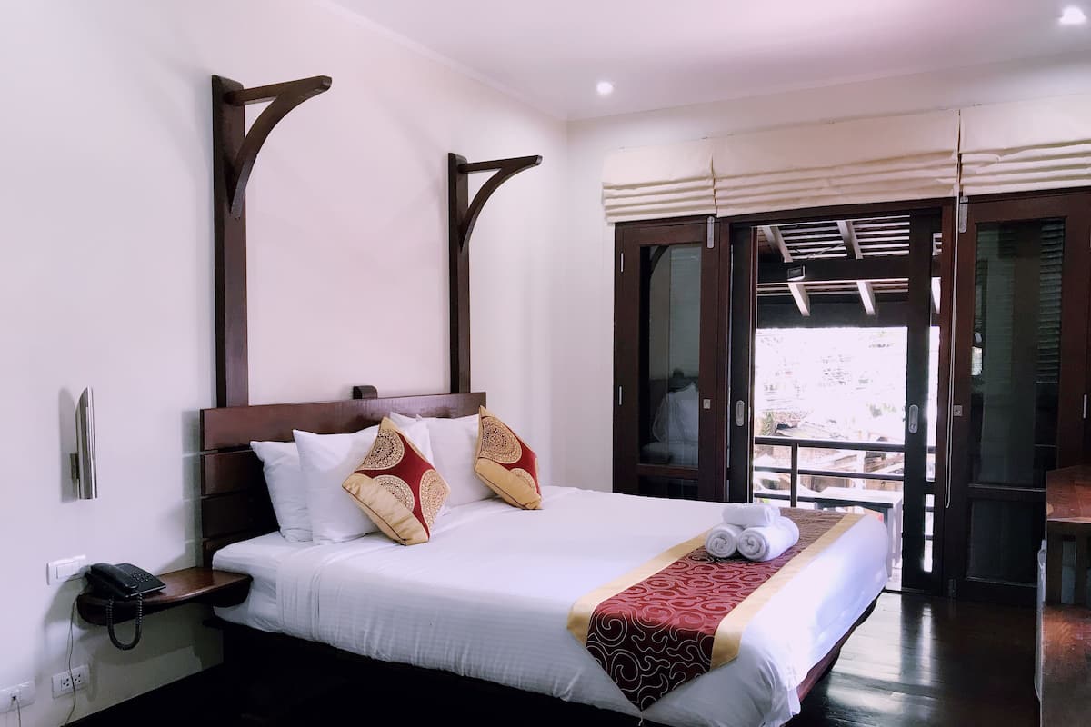 A neatly made bed with white linens and decorative pillows, a bedside telephone, and a wooden nightstand.