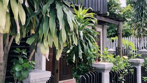 A traditional wooden house with a tiled entrance, surrounded by lush greenery and a black metal fence. - Ancient Luang Prabang Hotel (Luang Prabang)