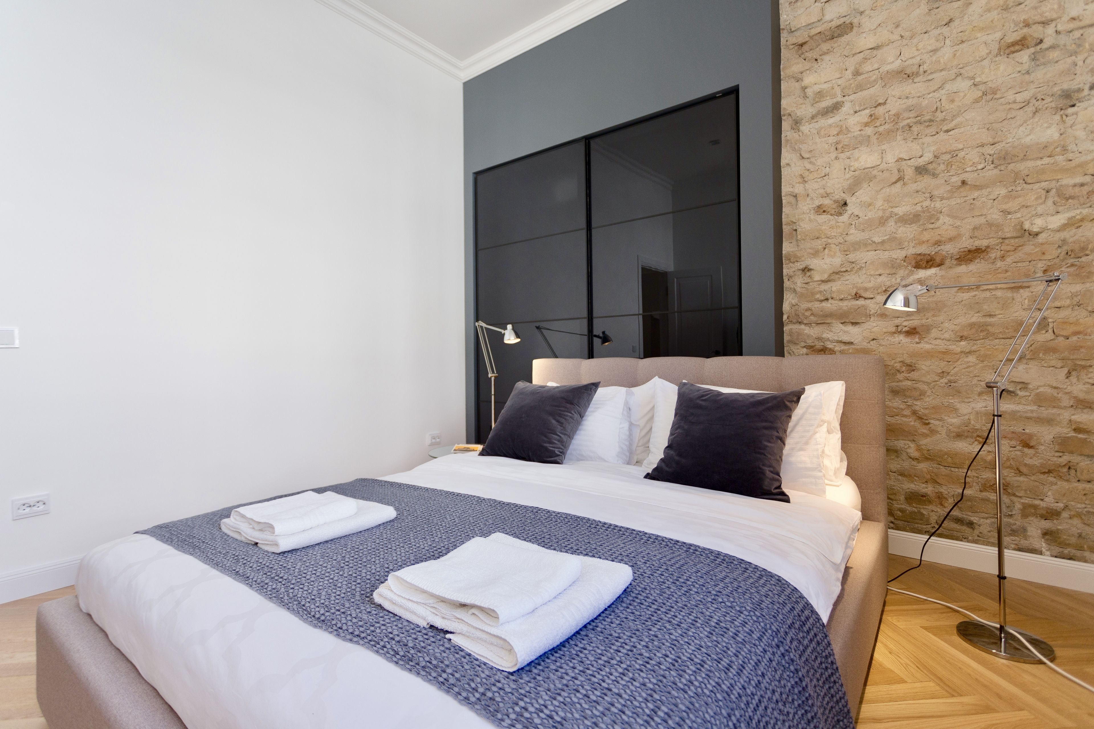 Une chambre moderne avec un grand lit, une tête de lit sombre et un mur en briques.