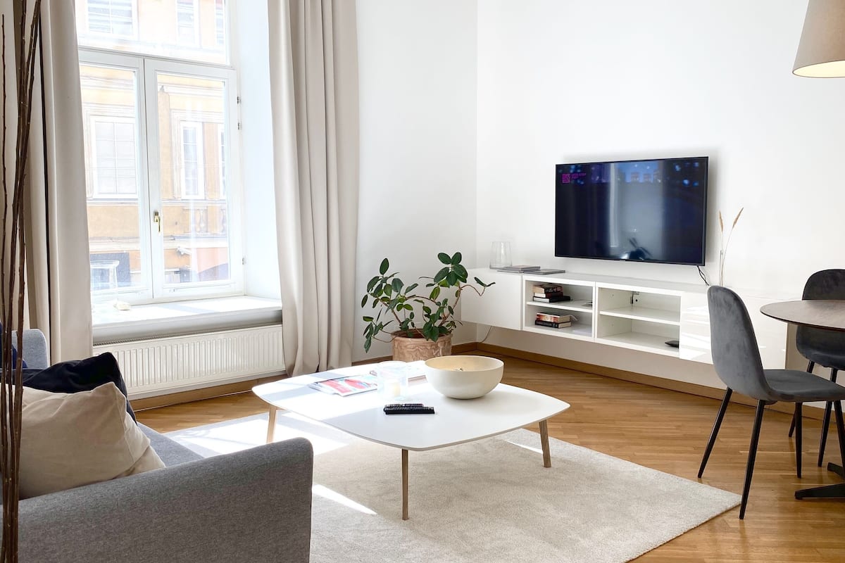 Moderni olohuone, jossa on sohva, sohvapöytä, televisio ja ruokailutila.
