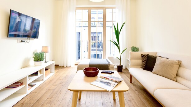 A modern living room with a sofa, a coffee table, a TV, and a large window with curtains. - Vilnius Apartments & Suites - Town Hall (Vilnius)