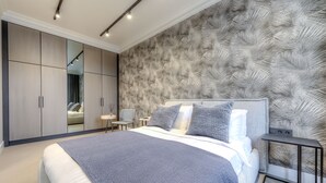 A modern bedroom with a large bed, a wardrobe, a nightstand, and a wall with a leaf pattern. - Vilnius Apartments & Suites - Town Hall (Vilnius)