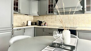A modern kitchen with grey cabinetry, a round dining table, and a vase with decorative branches. - Vilnius Apartments & Suites - Town Hall (Vilnius)