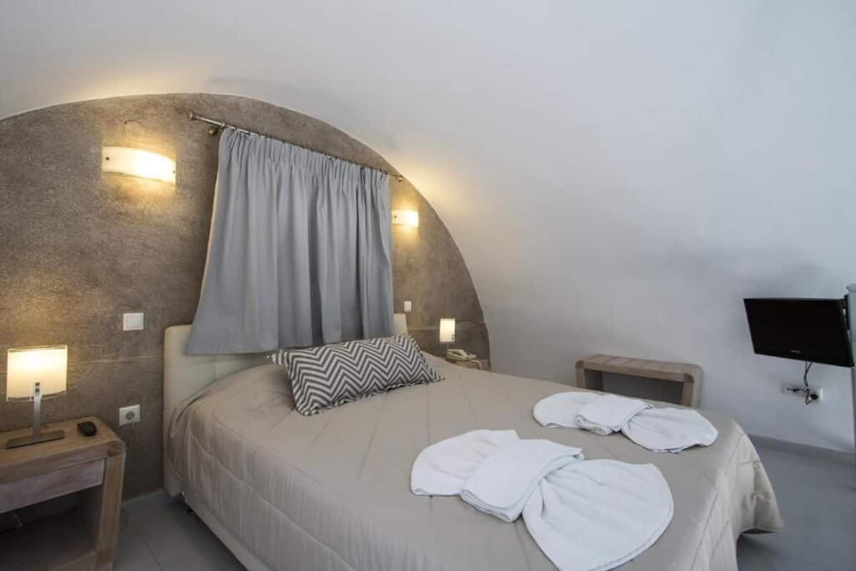 Un dormitorio moderno con techo curvo, una cama con almohada a rayas, mesitas de noche con lámparas y un televisor de pantalla plana.