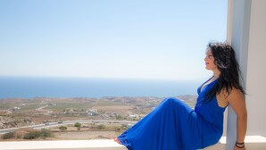 Una donna con un abito blu seduta su un balcone con vista sul mare e una strada.