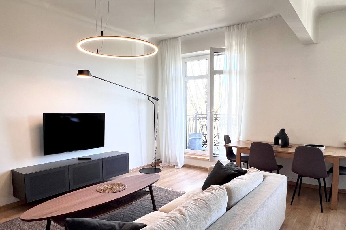 A modern living room with a sofa, a TV, a dining table, and a floor lamp.