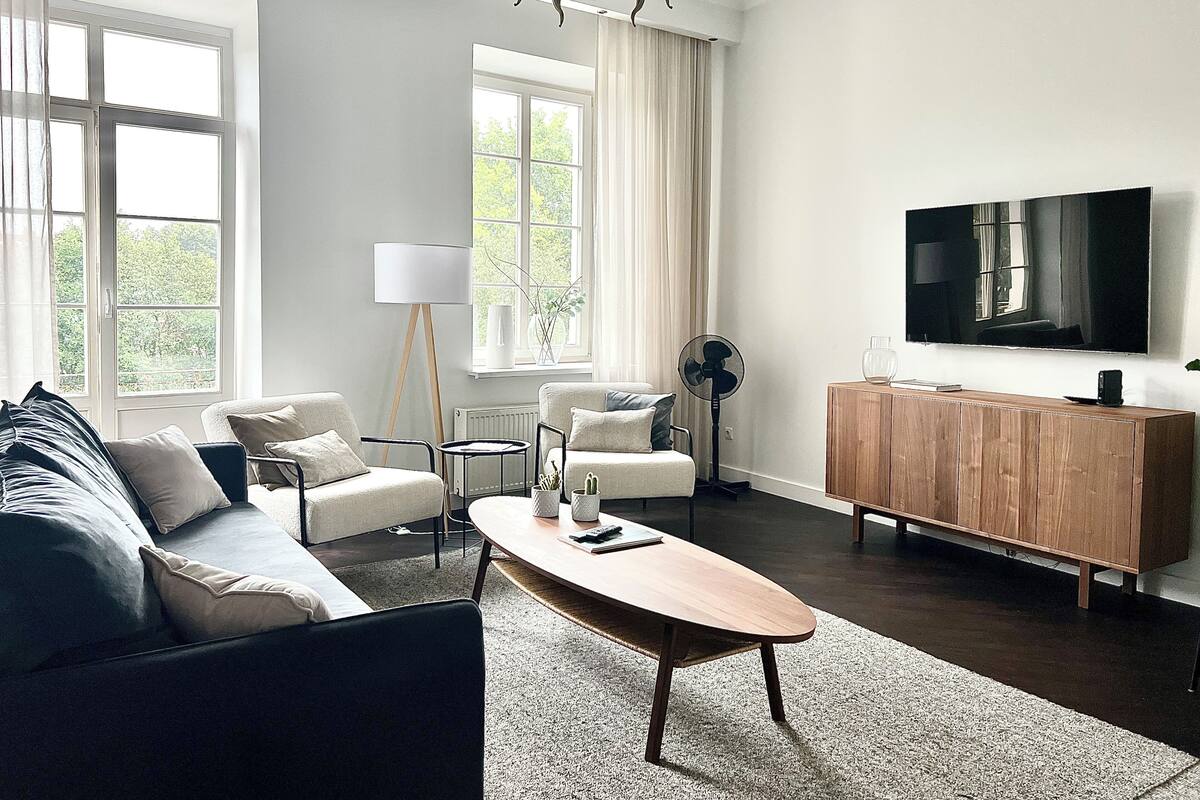 A modern living room with a sofa, armchairs, a coffee table, a TV, and a wooden cabinet.