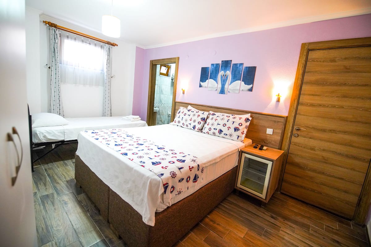 A bedroom with a large bed, a smaller bed, a nightstand, a wooden wardrobe, and a mirror.