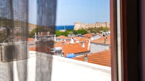 A view through a window with a curtain, featuring a coastal cityscape with buildings and a fort. - Bozcaada Hotel Vitis (Bozcaada)