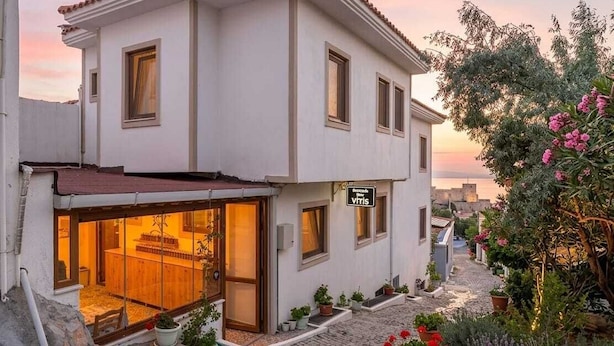 A two-story building with a visible restaurant on the ground floor, a paved courtyard, and a view of the sea in the background. - Bozcaada Hotel Vitis (Bozcaada)