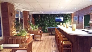 Un área de bar con mobiliario de madera, una mesa de billar y una pantalla de televisión en la pared.