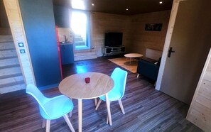 A cozy room with a wooden floor, a round table with two chairs, a TV, and a small sofa. - Glamping Terre & Mer (Binic-Etables-sur-Mer)
