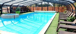 A covered swimming pool with lounge chairs and potted plants. - Glamping Terre & Mer (Binic-Etables-sur-Mer)