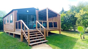 A wooden cabin with a glass door, a wooden deck, and a staircase leading to the entrance.