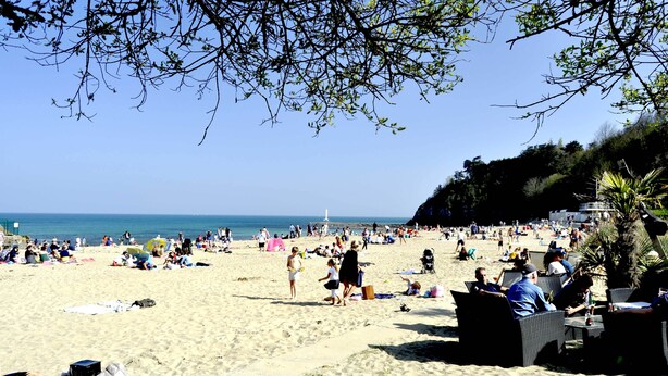 Una playa concurrida, gente tomando el sol y paseando.