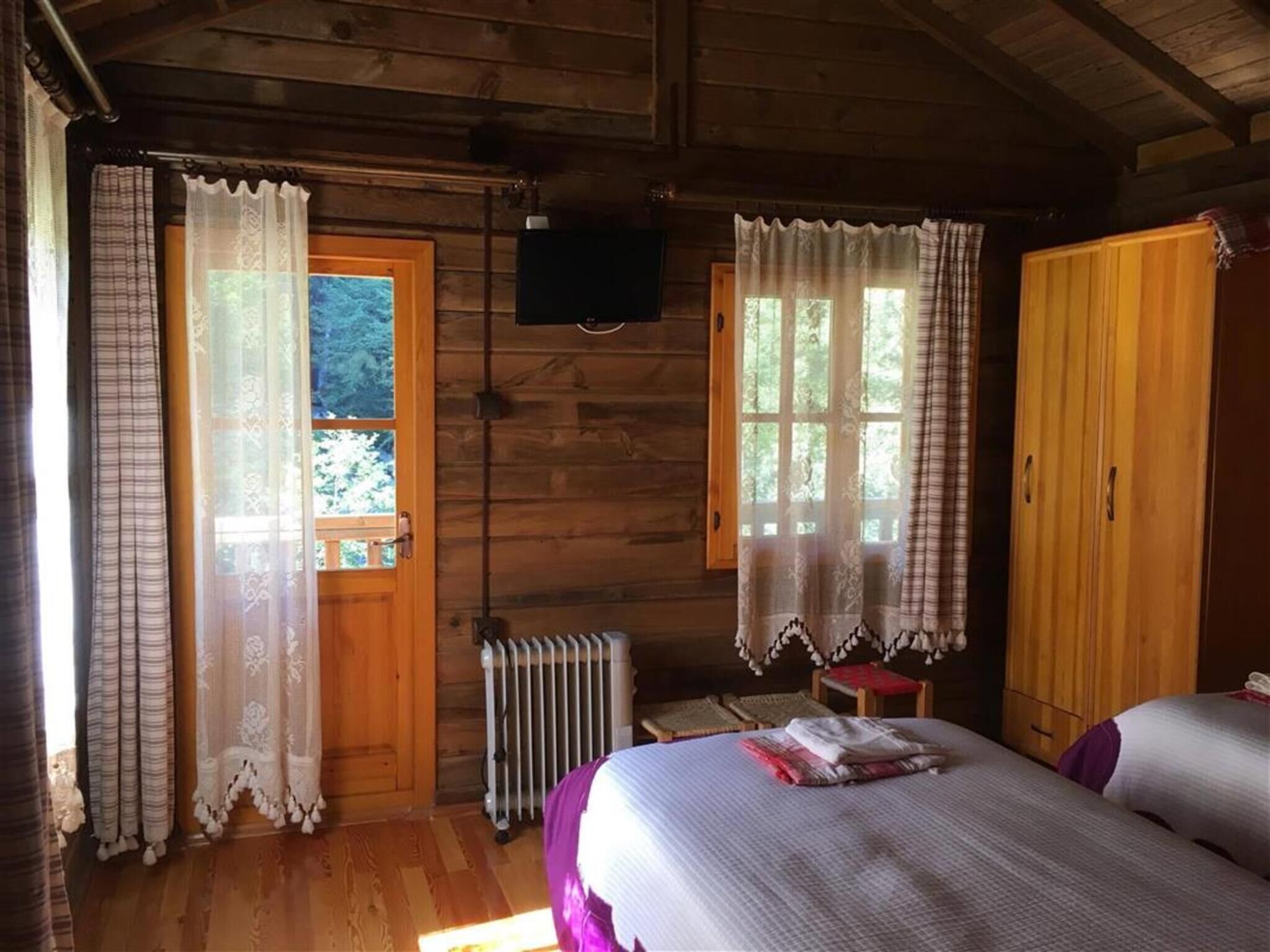 Une chambre dans un chalet en bois, avec deux lits, un radiateur et un téléviseur fixé au mur.