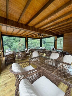 A spacious wooden deck with wicker furniture and large windows offering a view of the forest. - Mencuna Konaklari (Arhavi)