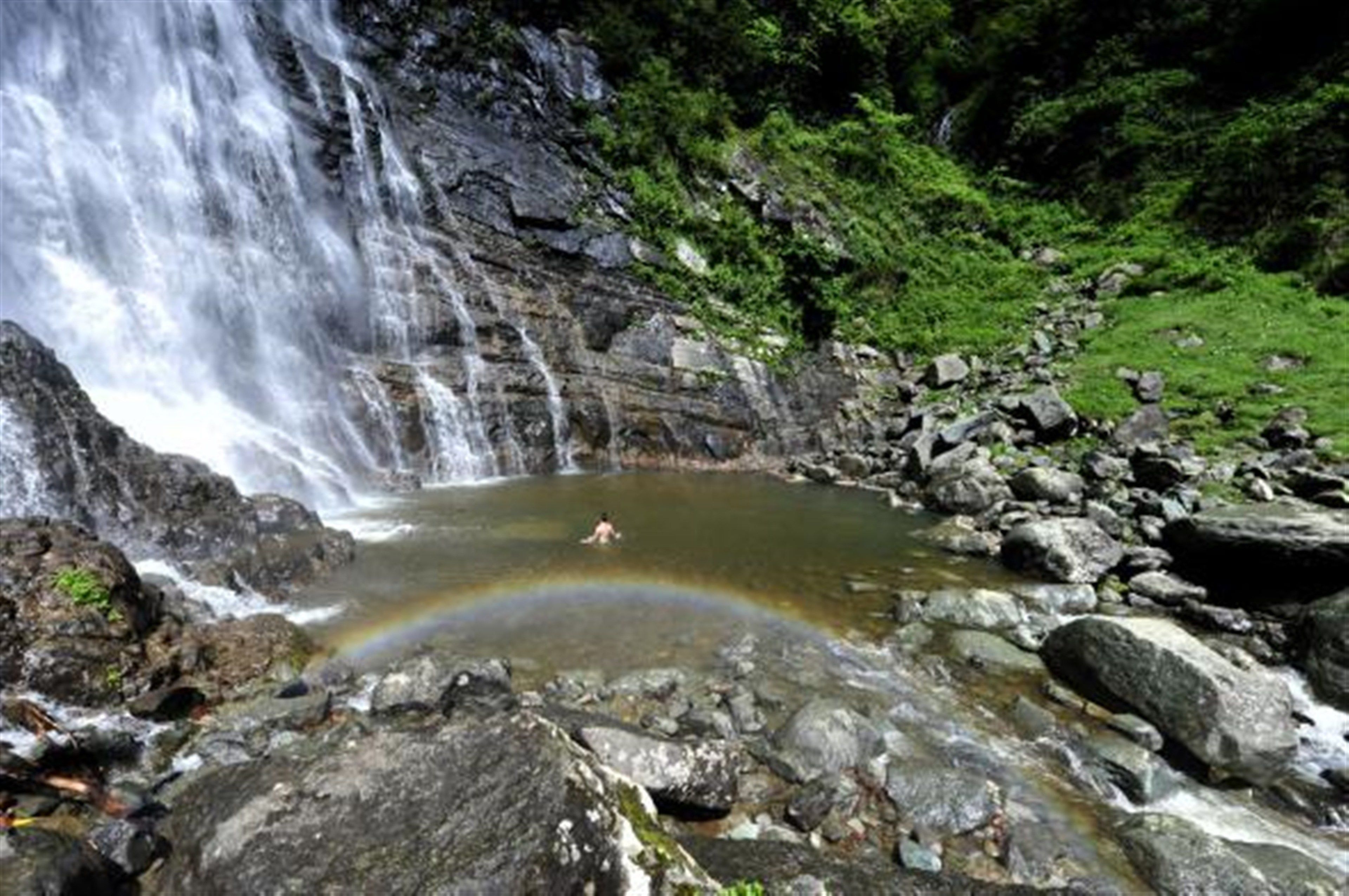 A waterfall cascading into a pool surrounded by rocks and greenery.