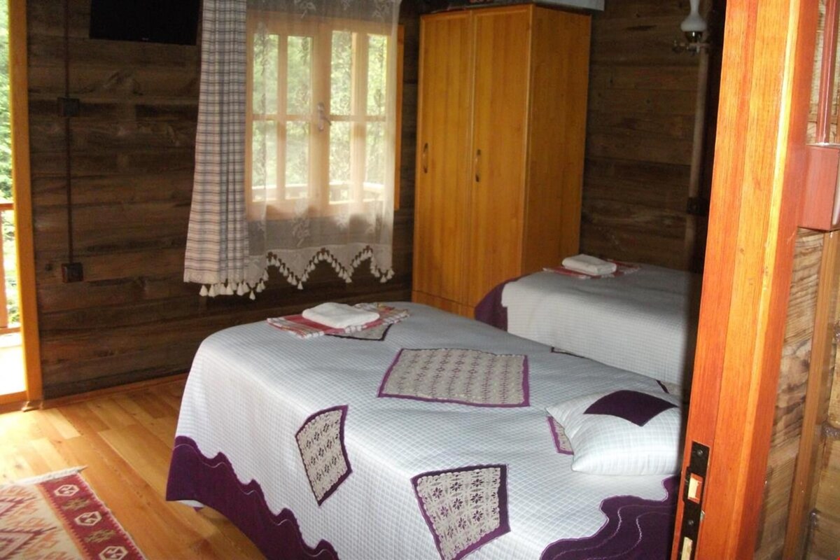 A cabin-style room with two beds, a wooden wardrobe, and a window with curtains.