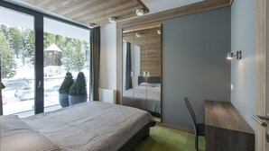 A modern hotel room with a large bed, a desk, and a view of a snowy landscape through large windows. - Apparthotel Silbersee (Stadl-Predlitz)
