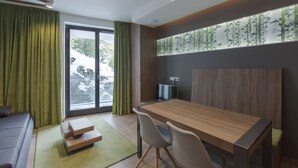 A modern room with a wooden dining table, two chairs, a sofa, and a large window with curtains. - Apparthotel Silbersee (Stadl-Predlitz)