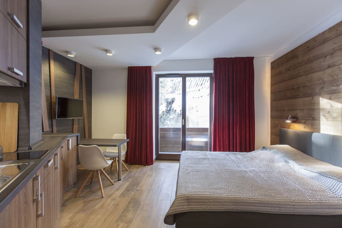 A modern hotel room with a bed, a desk, and a kitchenette.