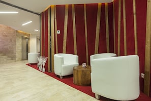 Un vestíbulo con alfombra roja, sofás blancos, una mesita de madera y una pared de piedra.