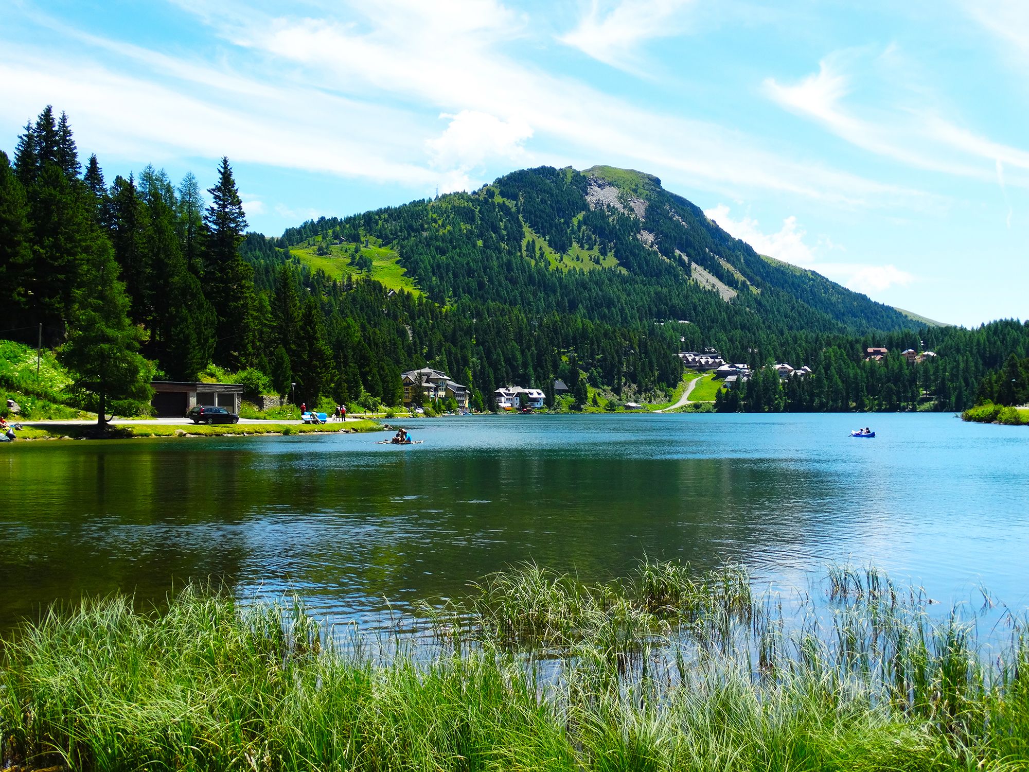 A serene lake with boats, surrounded by lush greenery and a mountain in the background.