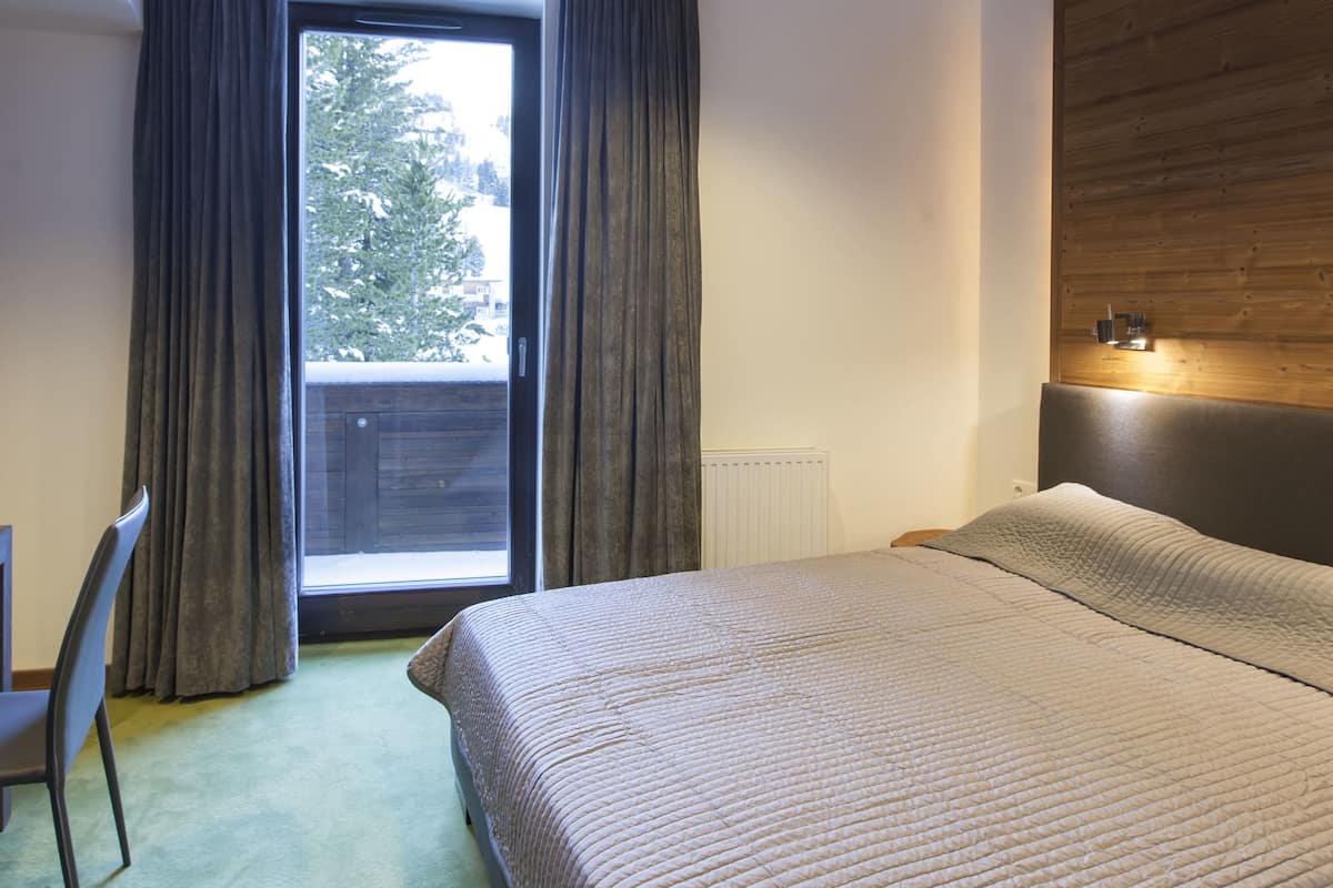 A bedroom with a bed, a chair, a window with curtains, and a wooden ceiling.