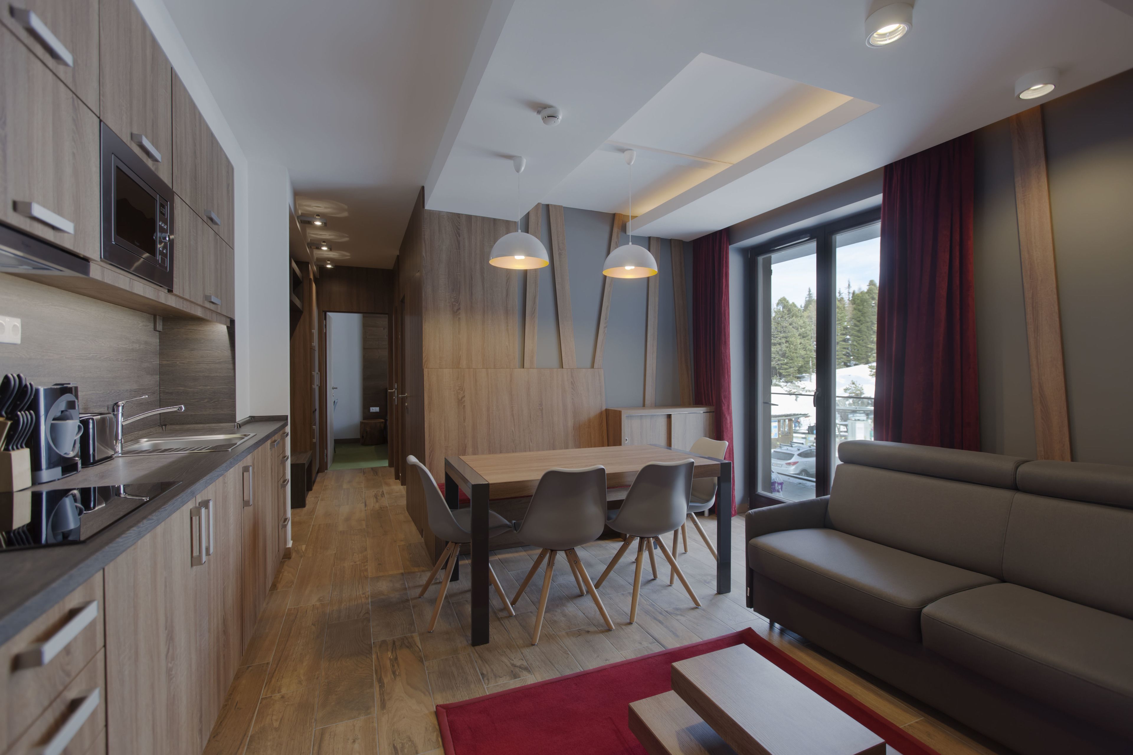 A modern kitchen with wooden cabinets, a dining area with a wooden table and chairs, and a living area with a sofa and large windows.