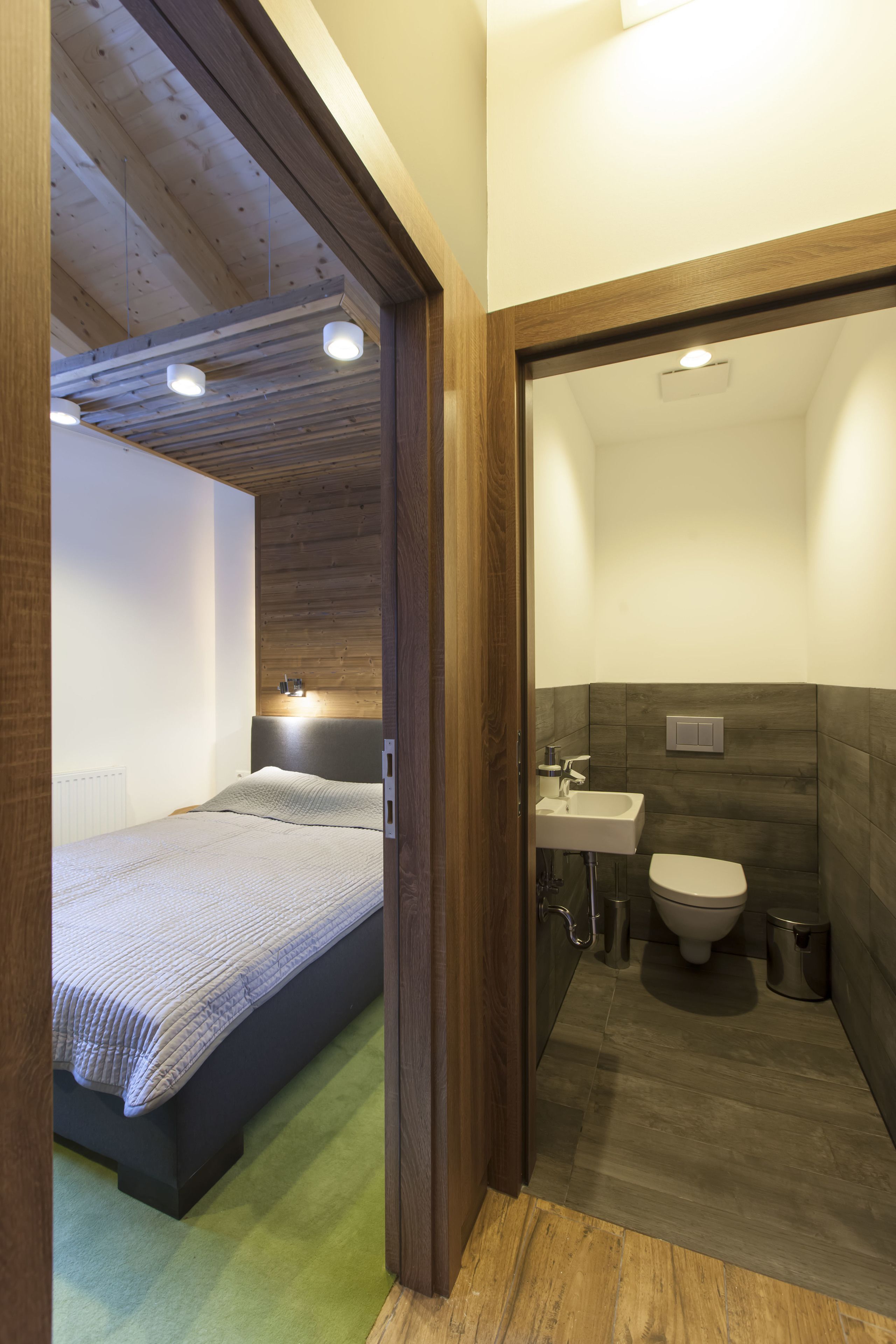 A bedroom with a bed, a bedside table, and a nightstand. There is a bathroom with a toilet, sink, and shower.
