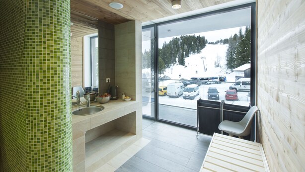 A modern bathroom with a green mosaic wall, a sink, and a window overlooking a snowy landscape. - Apparthotel Silbersee (Stadl-Predlitz)