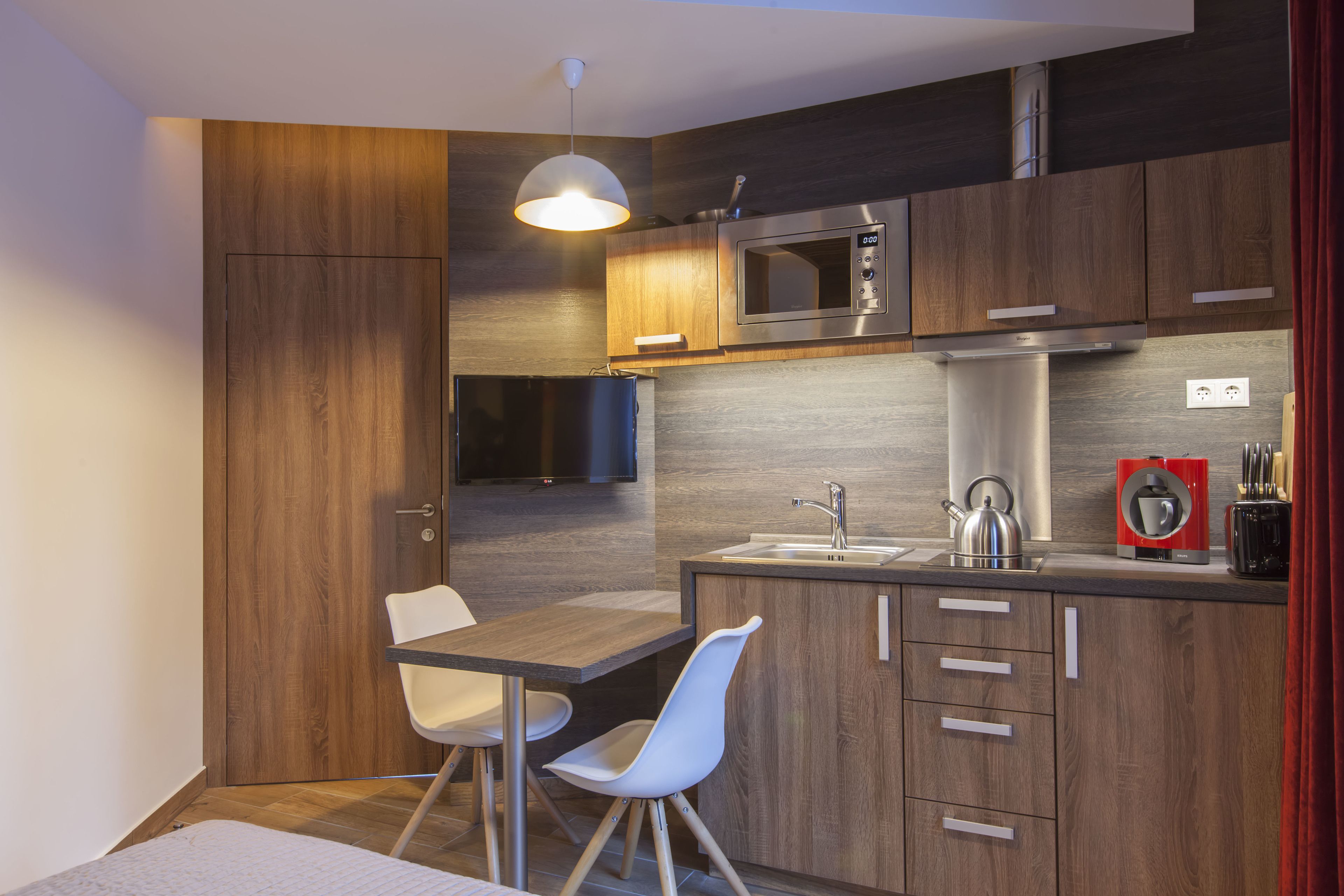 A compact kitchen with wooden cabinetry, a microwave, a sink, and a dining area with a chair.