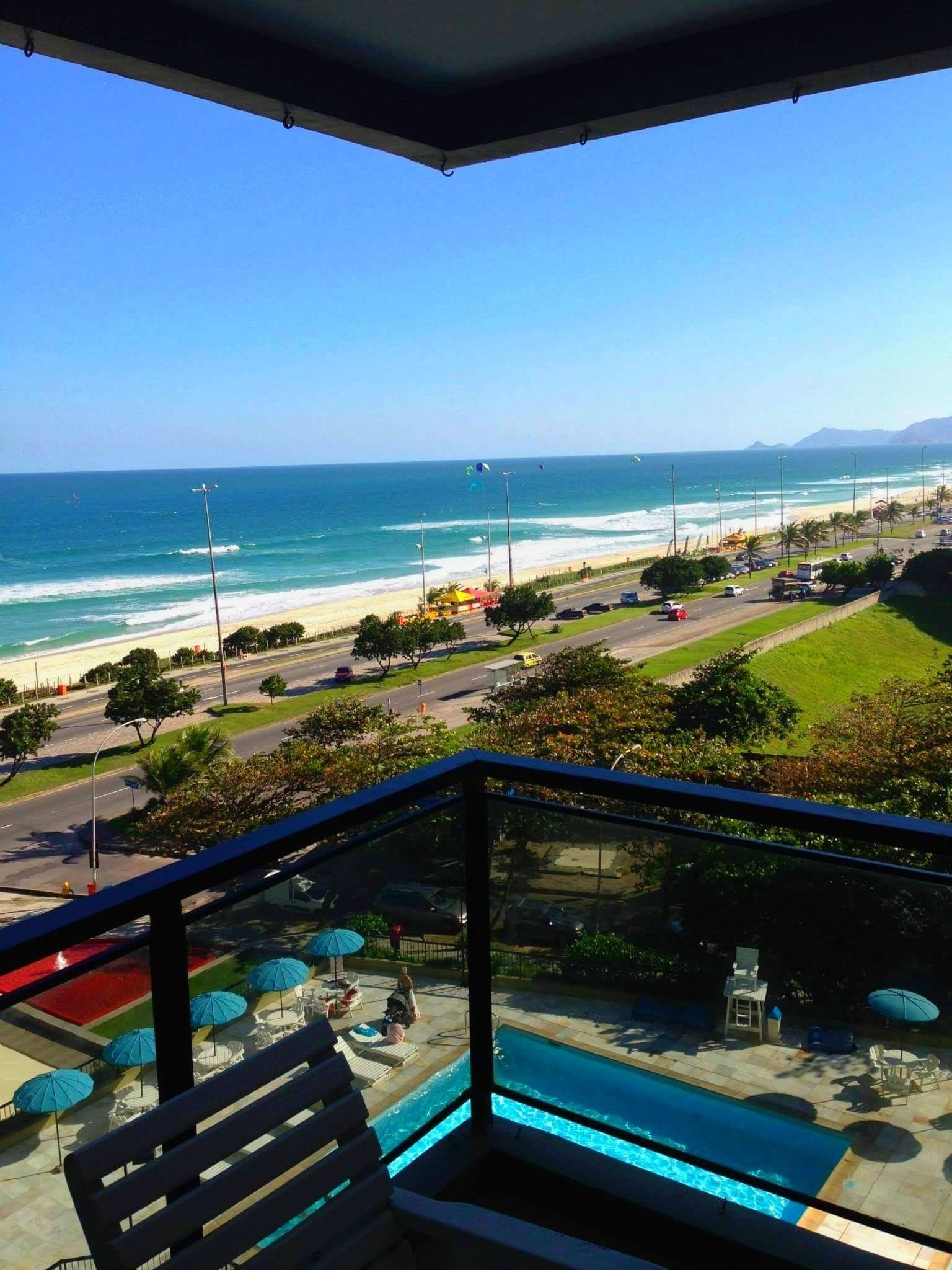 A balcony with a view of a swimming pool, beach, and ocean.