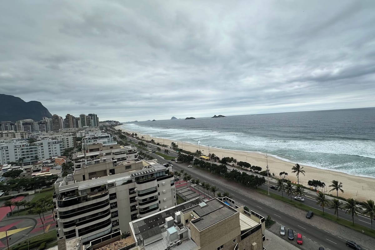 A coastal cityscape with a beach, high-rise buildings, and a road with vehicles.