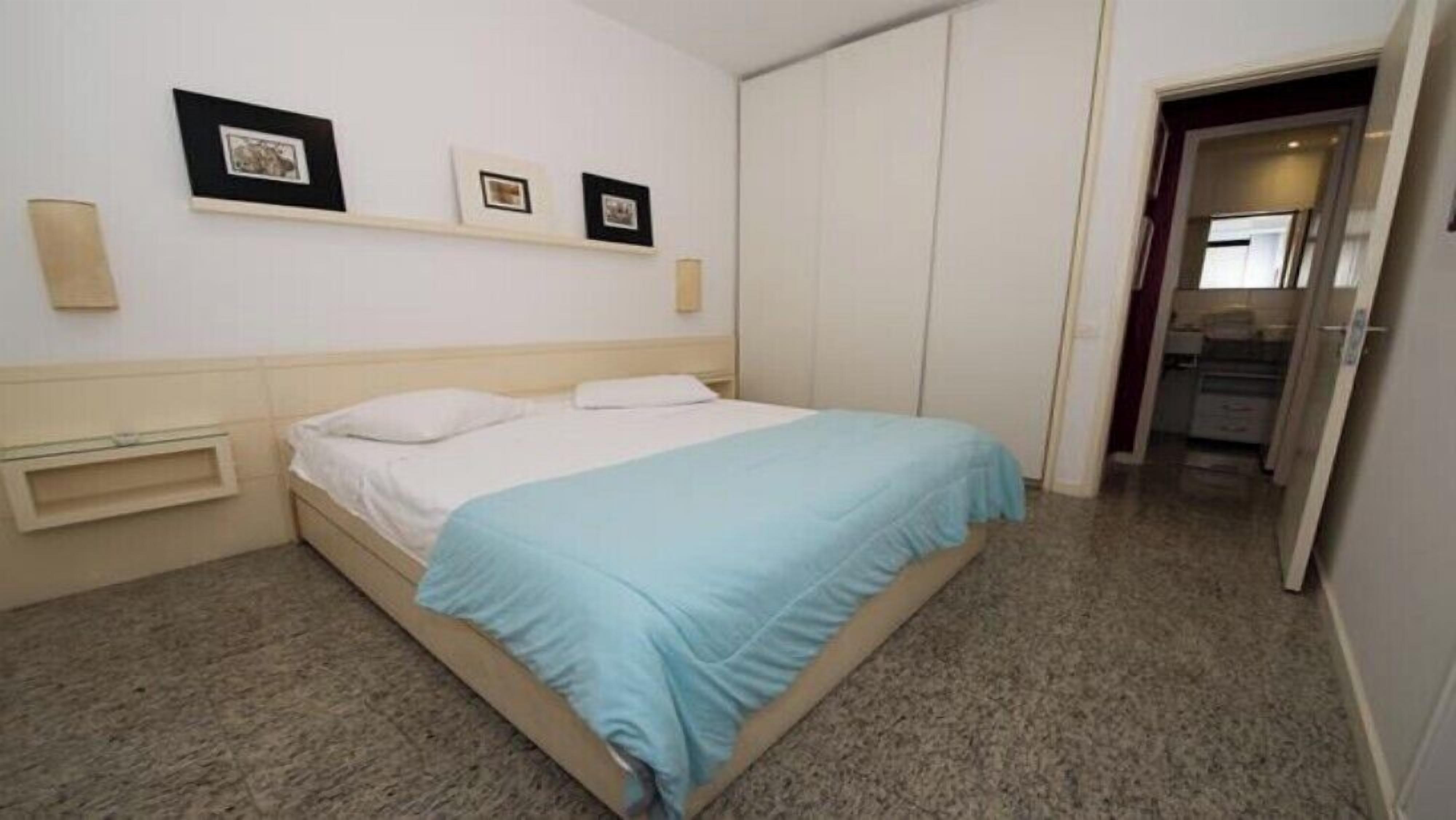 A bedroom with a bed, a bedside table, a wardrobe, and three framed pictures on the wall.
