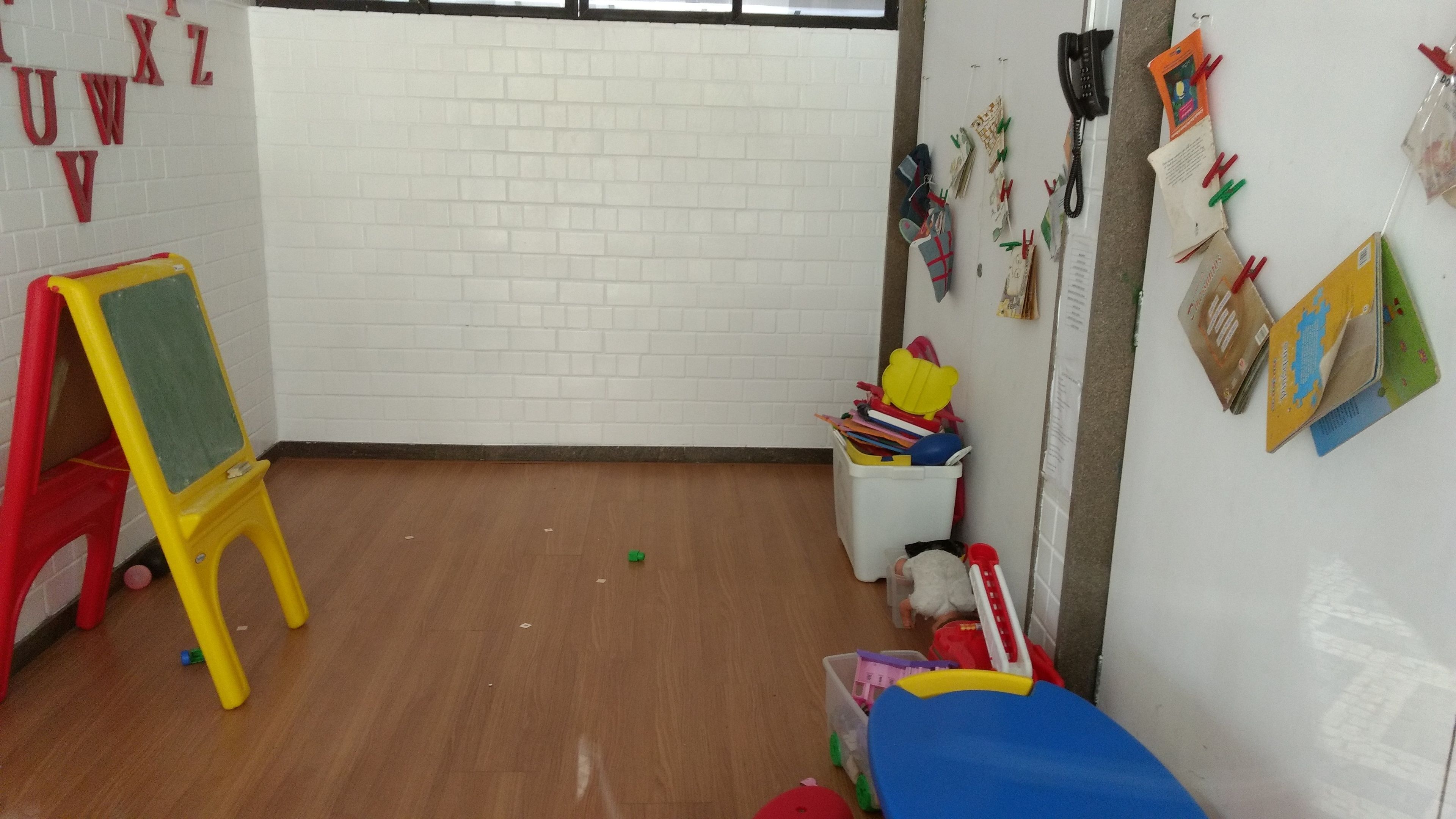 A room with a white brick wall, a wooden floor, a red and yellow easel, and a white storage bin filled with toys.