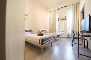 A hotel room with two beds, a desk, a chair, and a TV. - Romano Rooms (Catania)