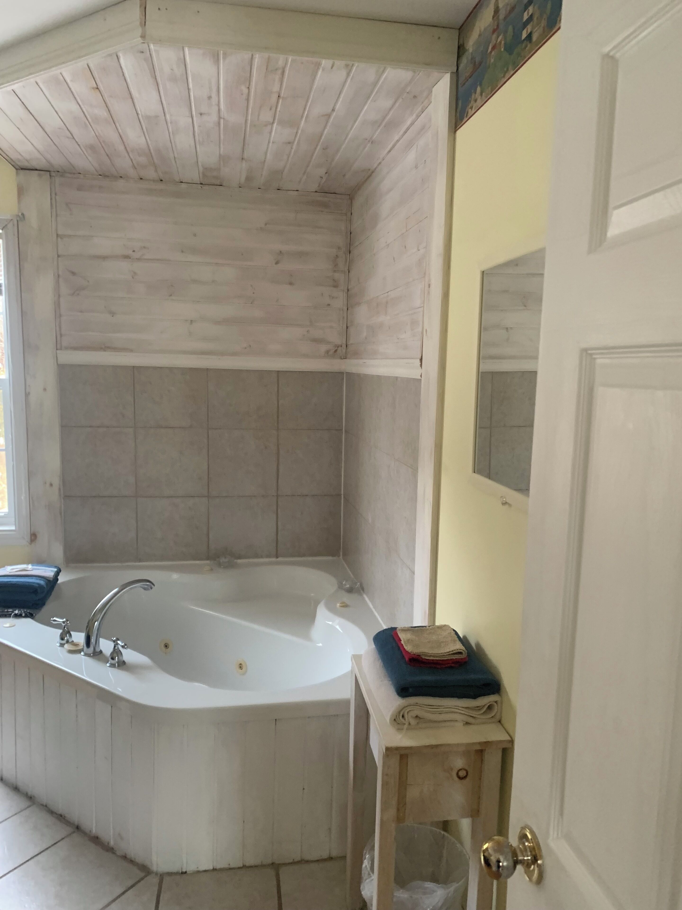 A bathroom with a freestanding bathtub, a small wooden stool with towels, and a door with a mirror.