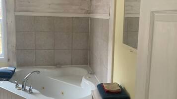 A bathroom with a freestanding bathtub, a small wooden stool with towels, and a door with a mirror.