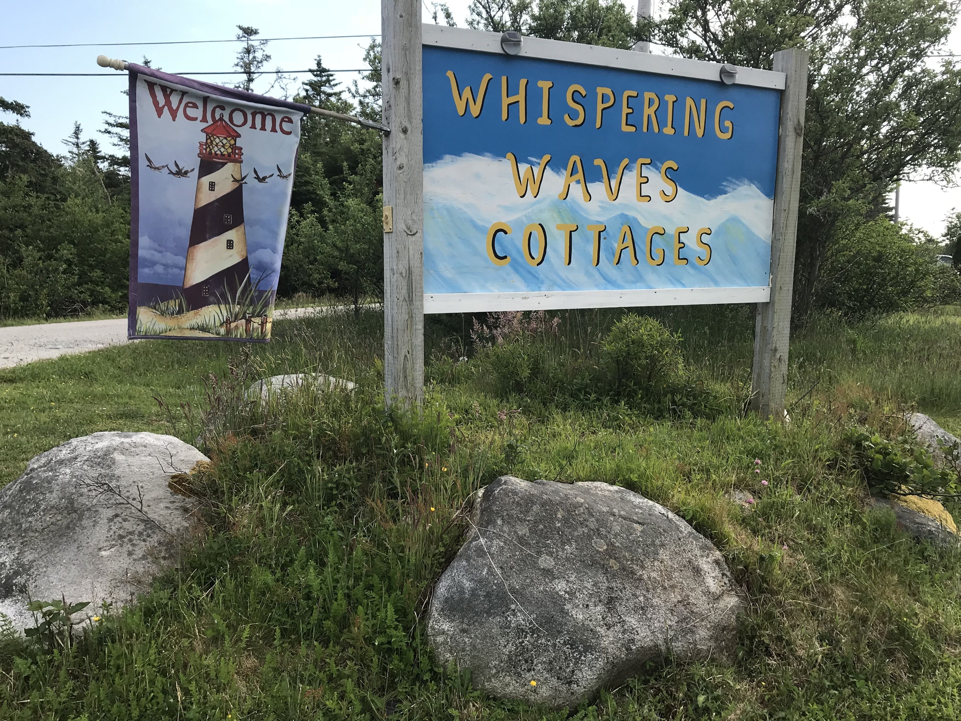 A sign for Whispering Waves Cottages with a lighthouse illustration.