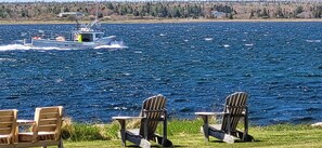 Un bateau sur une étendue d’eau, deux chaises en bois et une zone herbeuse.