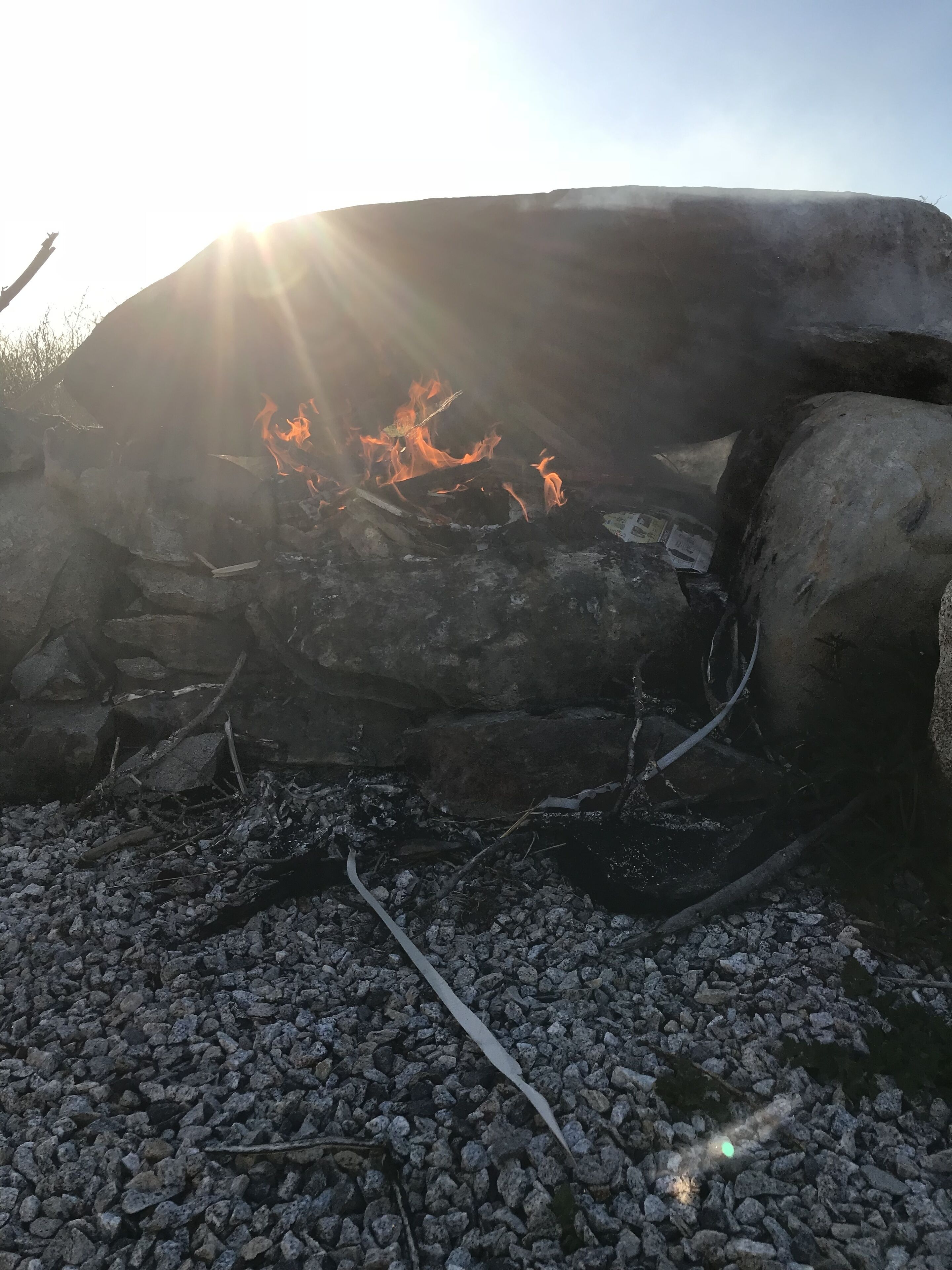 Un feu de camp entouré de rochers et de bûches, au milieu d’un paysage rocheux.