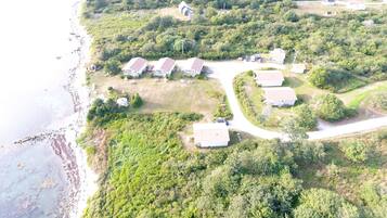 An aerial view of a coastal residential area with houses, a beach, and dense greenery.