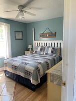A bedroom with a bed, a ceiling fan, a nightstand, a lamp, and a sign on the wall.