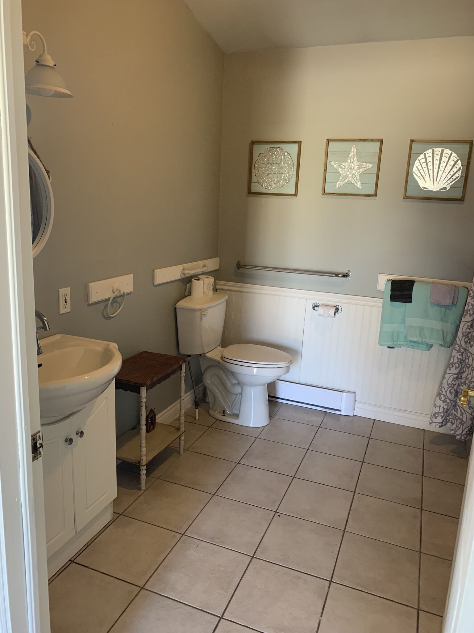A bathroom with a toilet, sink, and a small wooden stool. There are three framed wall decorations above the toilet.