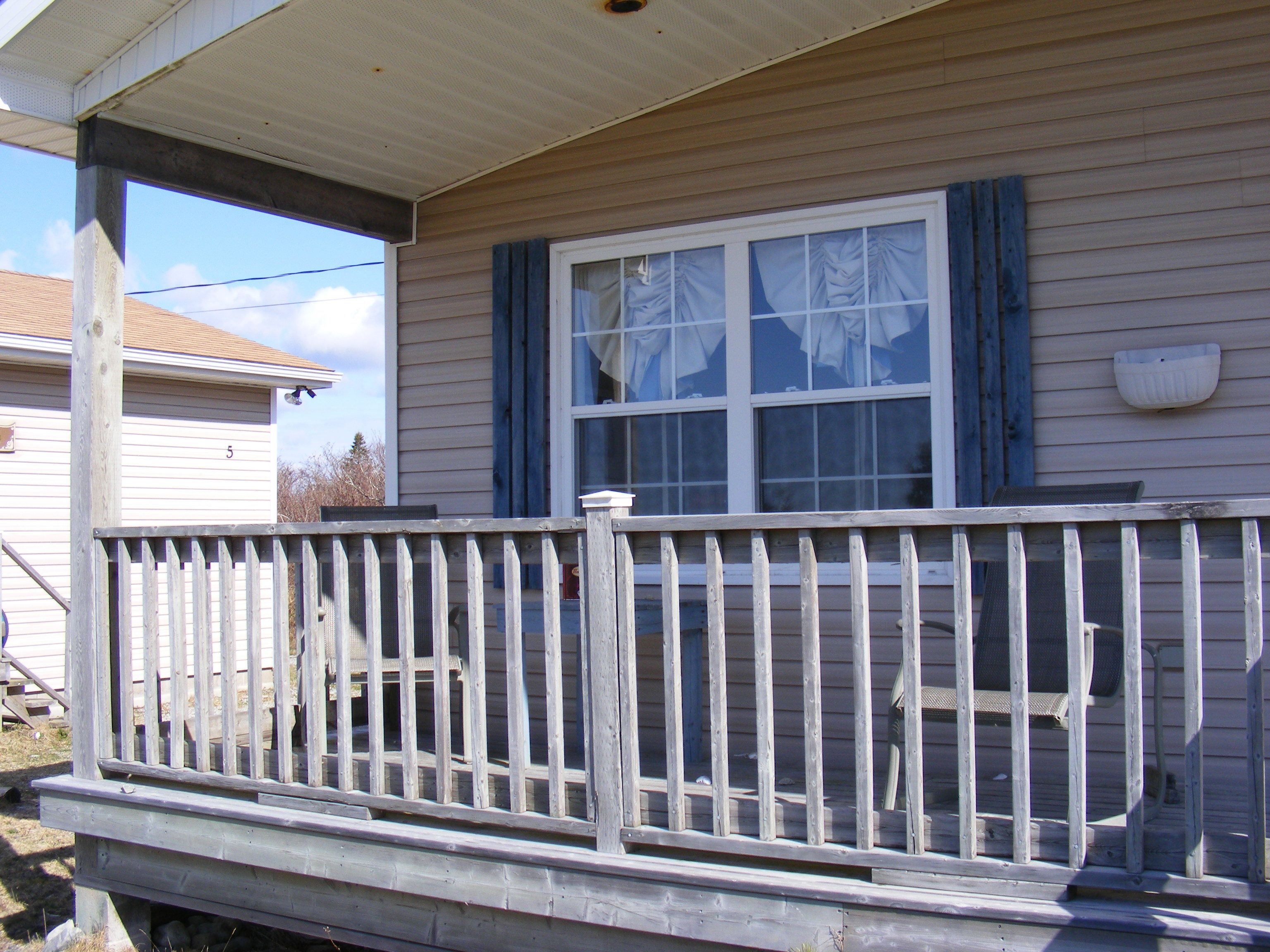 A house with a porch, a window with blue shutters, and a white mailbox on the wall.